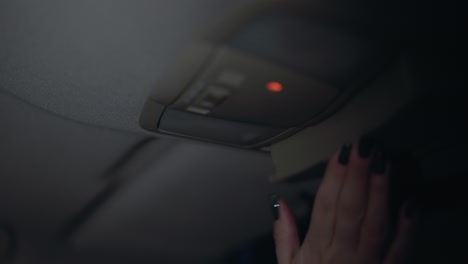 first-person view of a woman turning off the left car light at night. the interior light switch is being turned off, the woman's hand with black painted nails