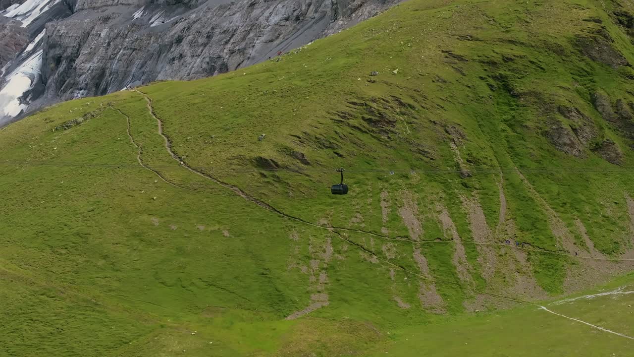 Gondola cable cars moving above the lush green valley of Grindelwald, Switzerland, aerial close up shot