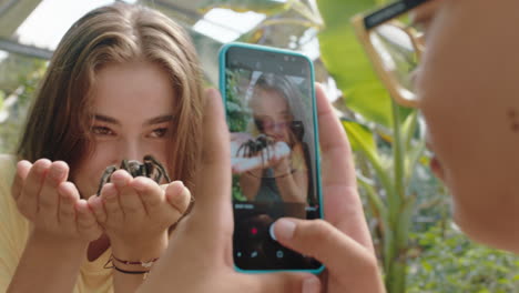 young girl holding tarantula spider with friend taking photo using smartphone sharing zoo excursion on social media learning about arachnids at wildlife sanctuary 4k