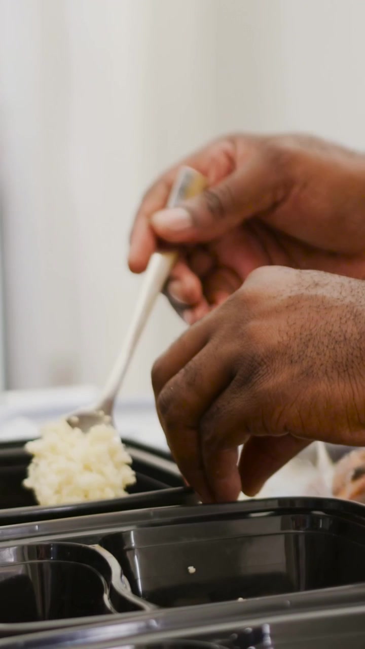 Video verticale: Mani di un uomo che dosano il riso con un cucchiaio, riempiendo vassoi di preparazione in cucina per i pasti.