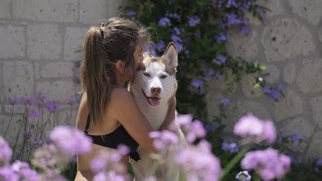 mujer husky y propietaria en un jardín lleno de flores