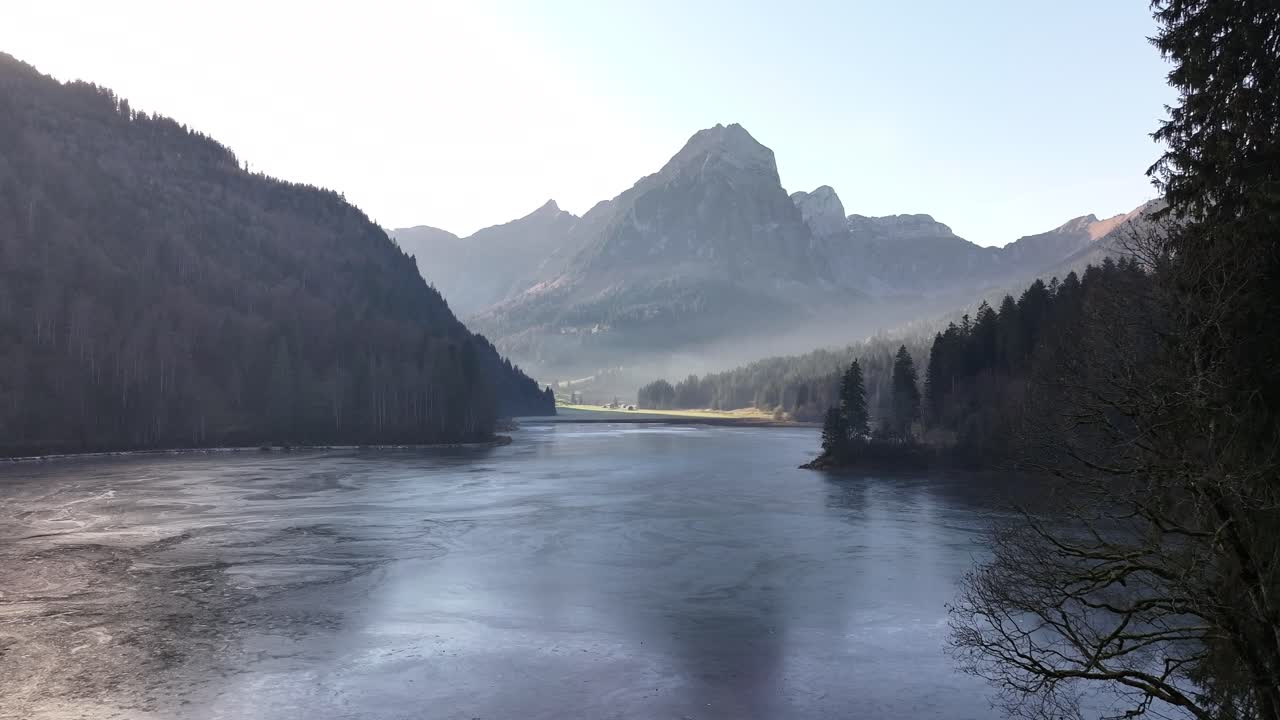 Aerial view of Obersee, an alpine lake nestled amidst the Swiss Alps. Misty mountains, lush forests, and a serene lake create a breathtaking landscape. Perfect for nature documentaries, travel videos.
