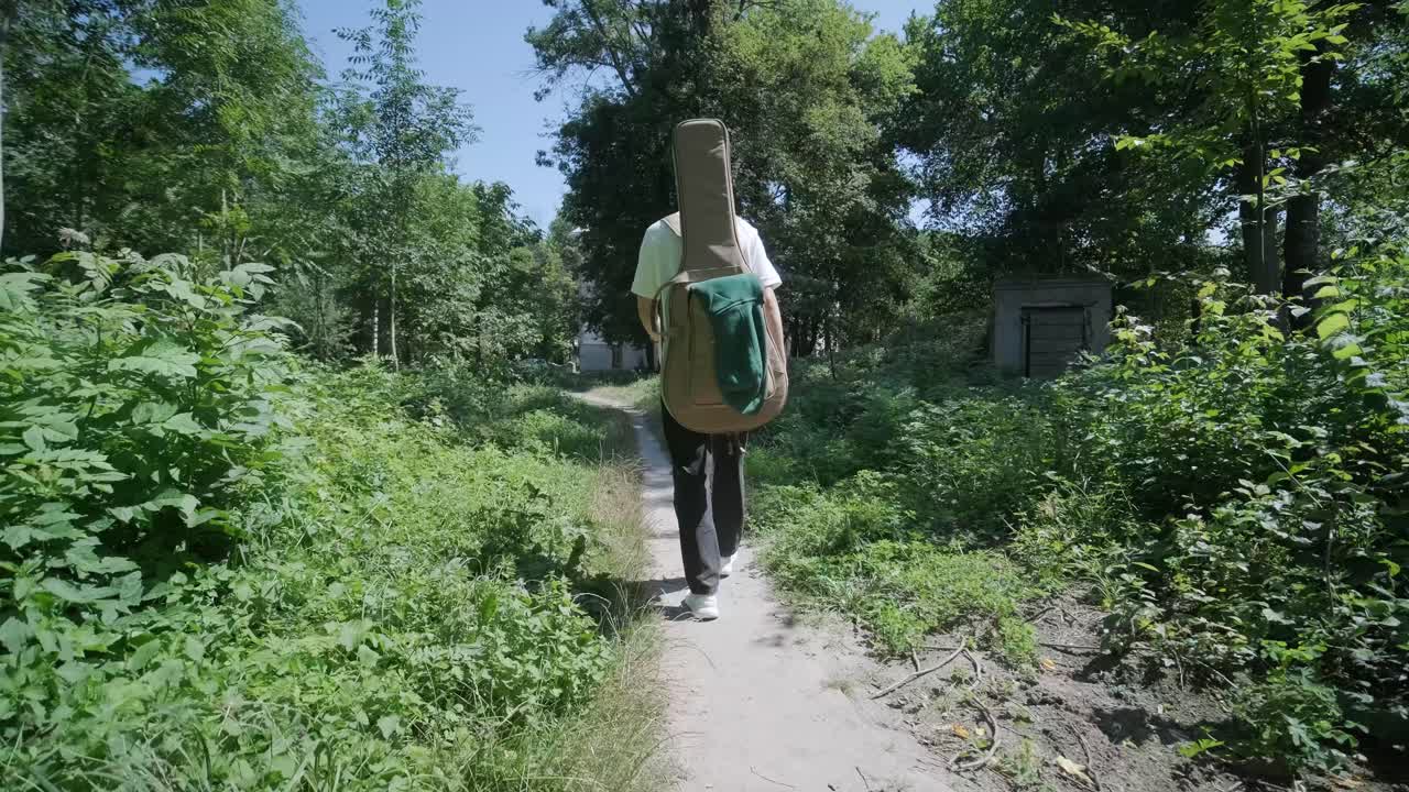joven caminando con la guitarra en la calle cerca del bosque