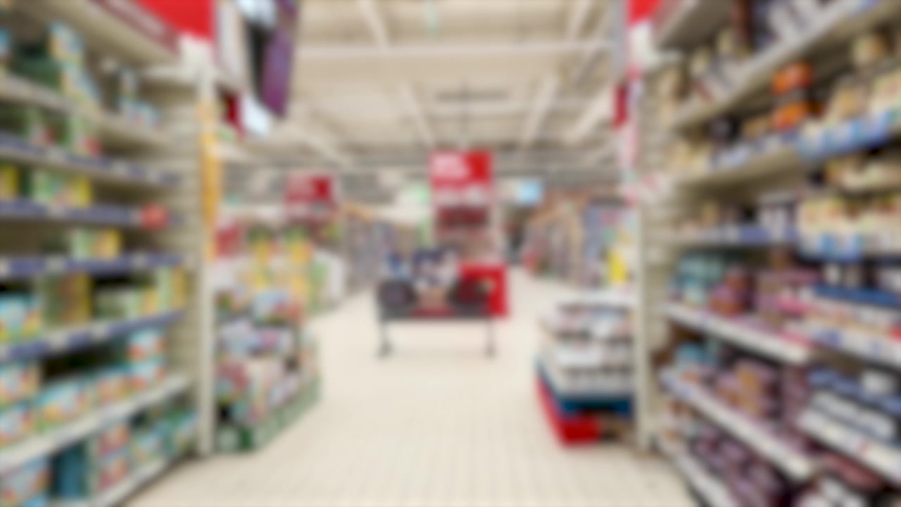 A blurred tracking shot moves forward through a brightly lit grocery store retail aisle