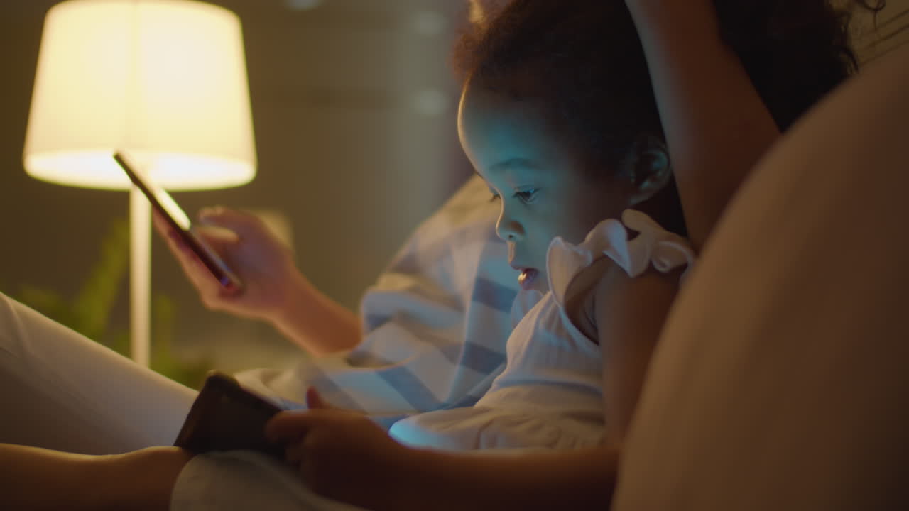 Asian Mother and Little Daughter Using Gadgets on Bed