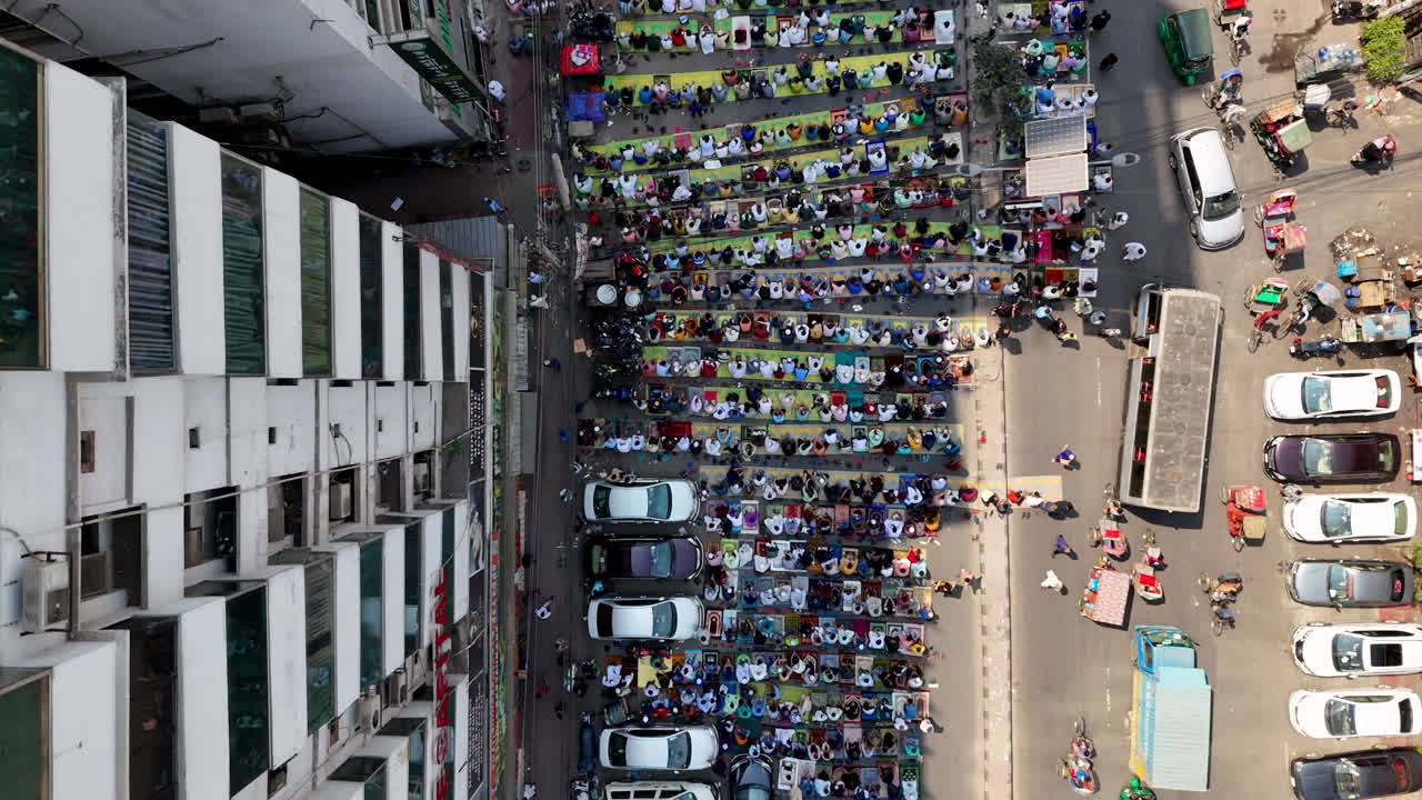 Cinematic aerial drone shot over muslims on the side of the street praying beside traffic in Dhaka, Bangladesh, downward angle