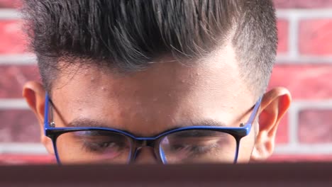 close-up of a young man with glasses working on a computer