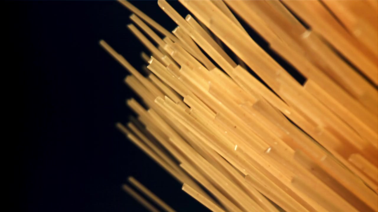 Spaghetti secchi che cadono al rallentatore su uno sfondo scuro.