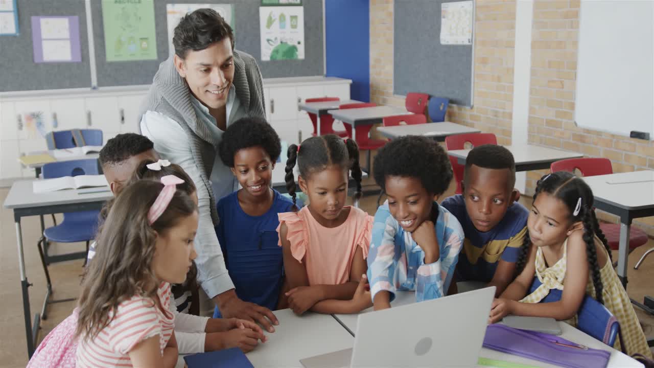 diverso maestro masculino feliz y niños usando computadora portátil en clase de escuela primaria, cámara lenta