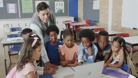 Happy-diverse-male-teacher-and-children-using-laptop-in-elementary-school-class,-slow-motion