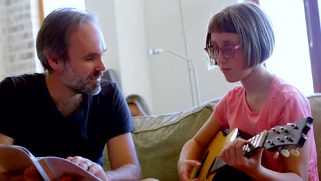 father helping her daughter to play guitar in living room 4k