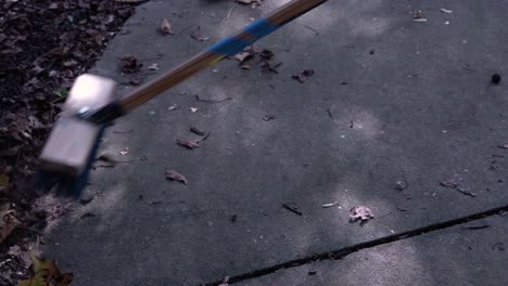 sweeping brown leaves off of a side walk using broom with wooden handle wrapped in tape