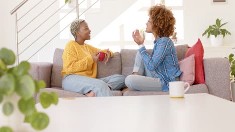 feliz pareja de lesbianas diversas hablando y bebiendo café en la sala de estar en cámara lenta