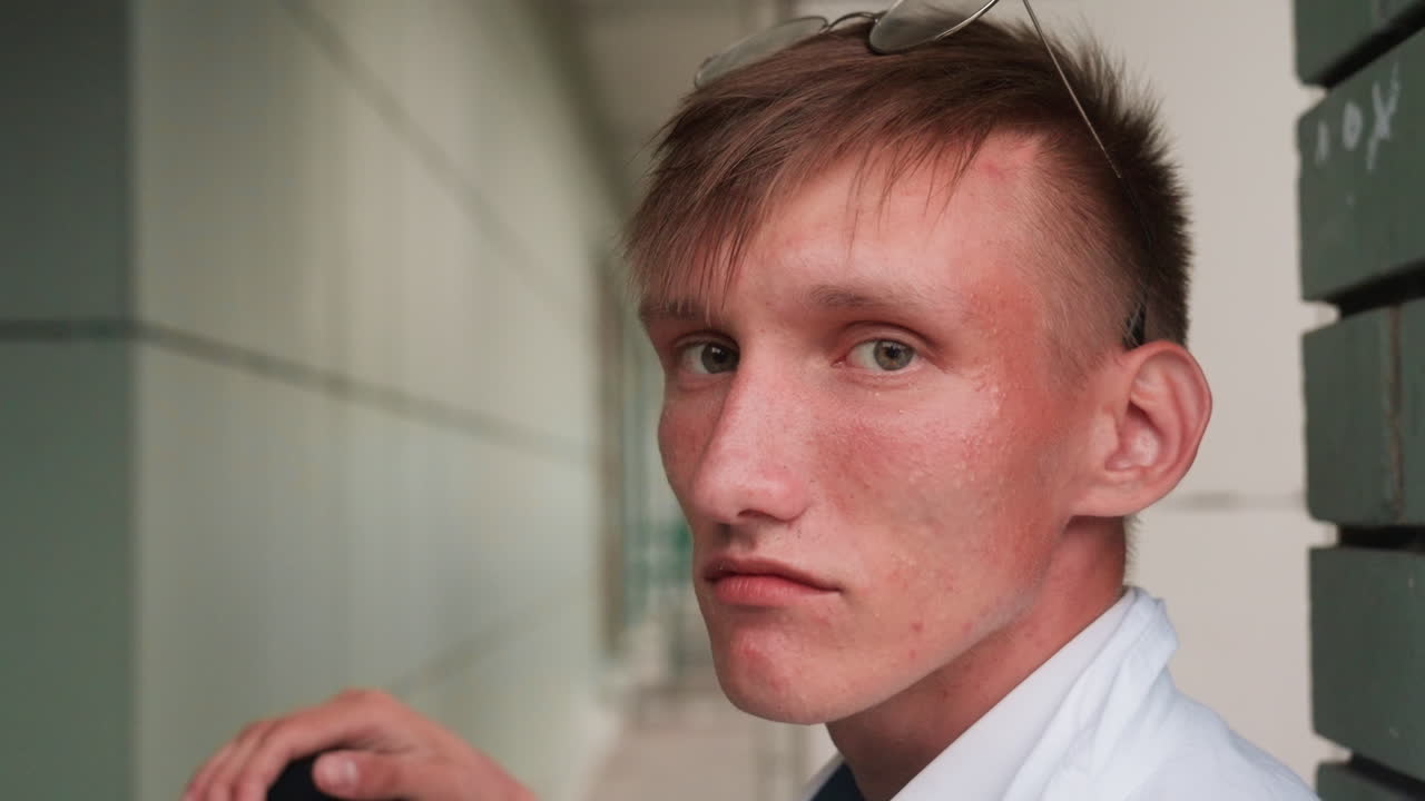 Close side view of young man in white shirt with glasses on head looking focused, reflecting calm expression of concentration, contemplation, and determination in outdoor setting