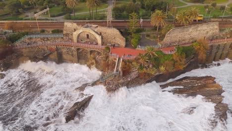 waves crashing against cliffs by the nervi walkway in genoa, italy, aerial view