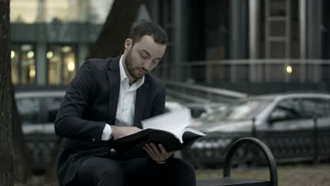 man is sitting on a bench in park and displeased reading business plan