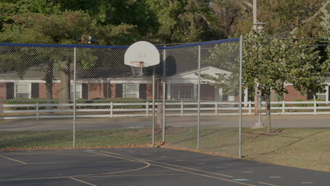 basketball hoop and outdoor court on school yard blacktop in autumn with a pan right revealing another basketball hoop