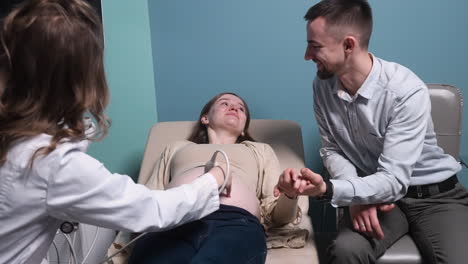 pregnant woman having ultrasound scan at the gynecologist office while loving husband holding her hand