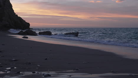 Wunderschöne-Strandlandschaft-Bei-Sonnenuntergang-Mit-Wellen-Und-Klippen-Im-Hintergrund-Bei-Ebbe