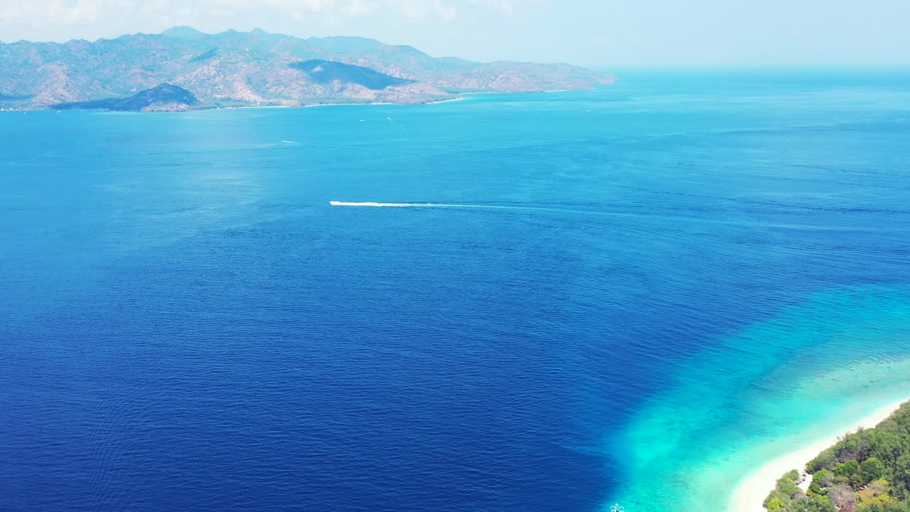 Boat sailing across blue sea stream between two shores of tropical islands with white exotic beaches on morning of Balinese coastline