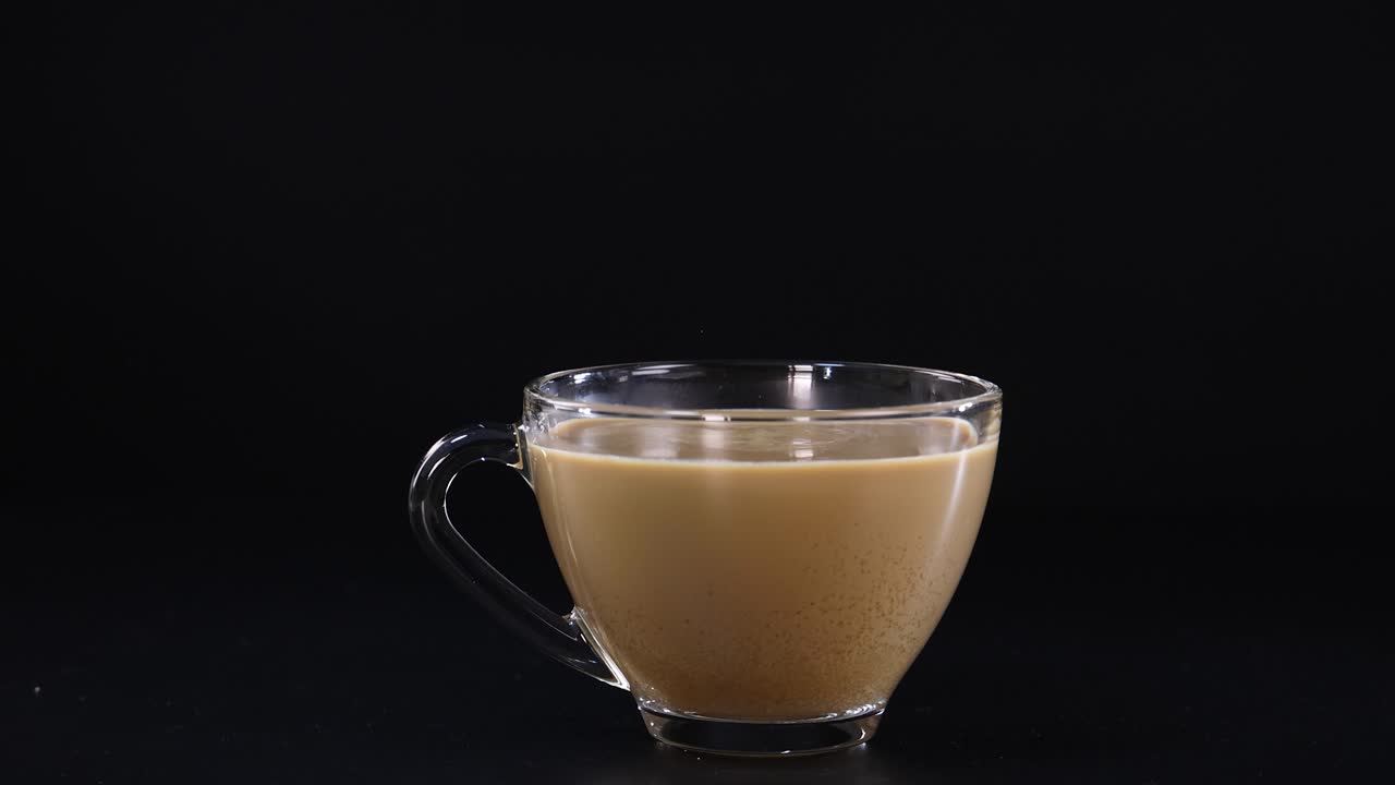 A sequence of sugar being poured into a glass cup of coffee against a dark backdrop, highlighting the contrast and motion