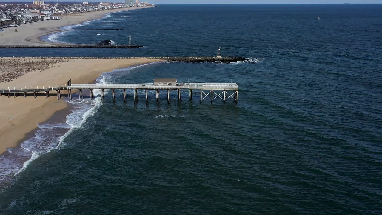 órbita aérea de una cabaña en un muelle en la playa de una pequeña ciudad turística en un día soleado