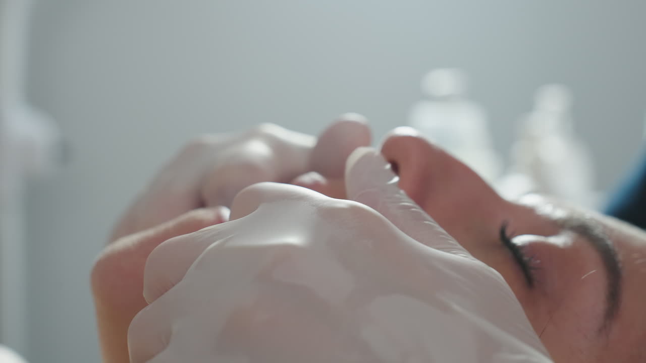 Close up of gloved hands gently pressing and smoothing lips of relaxed female client lying on spa bed with soft focus background conveying precise facial massage technique