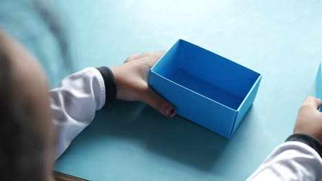 child's hands making a blue cardboard box