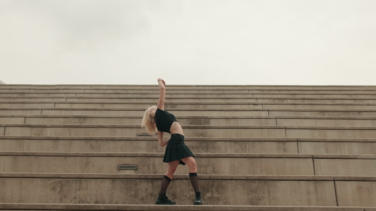 Giovane donna che esegue danza contemporanea su gradini di cemento urbani