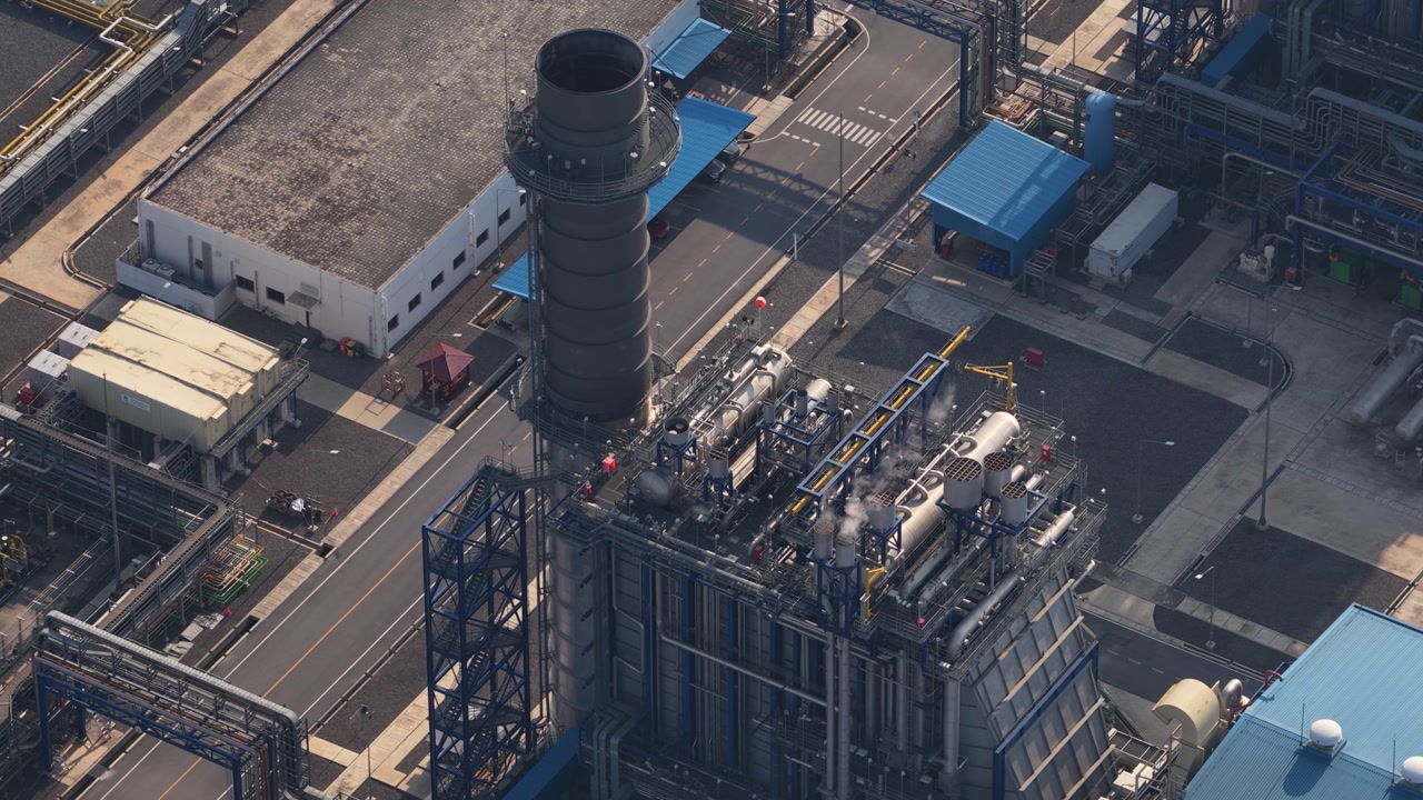 Aerial footage showing a large industrial power plant with pipelines and a smokestack, highlighting the infrastructure for energy production and distribution in a modern manufacturing facility
