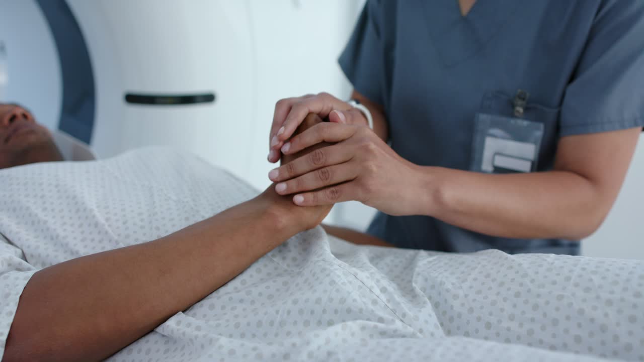 Nurse is reaching in, clasping and rubbing patient's right wrist, steadying for scan in scan room