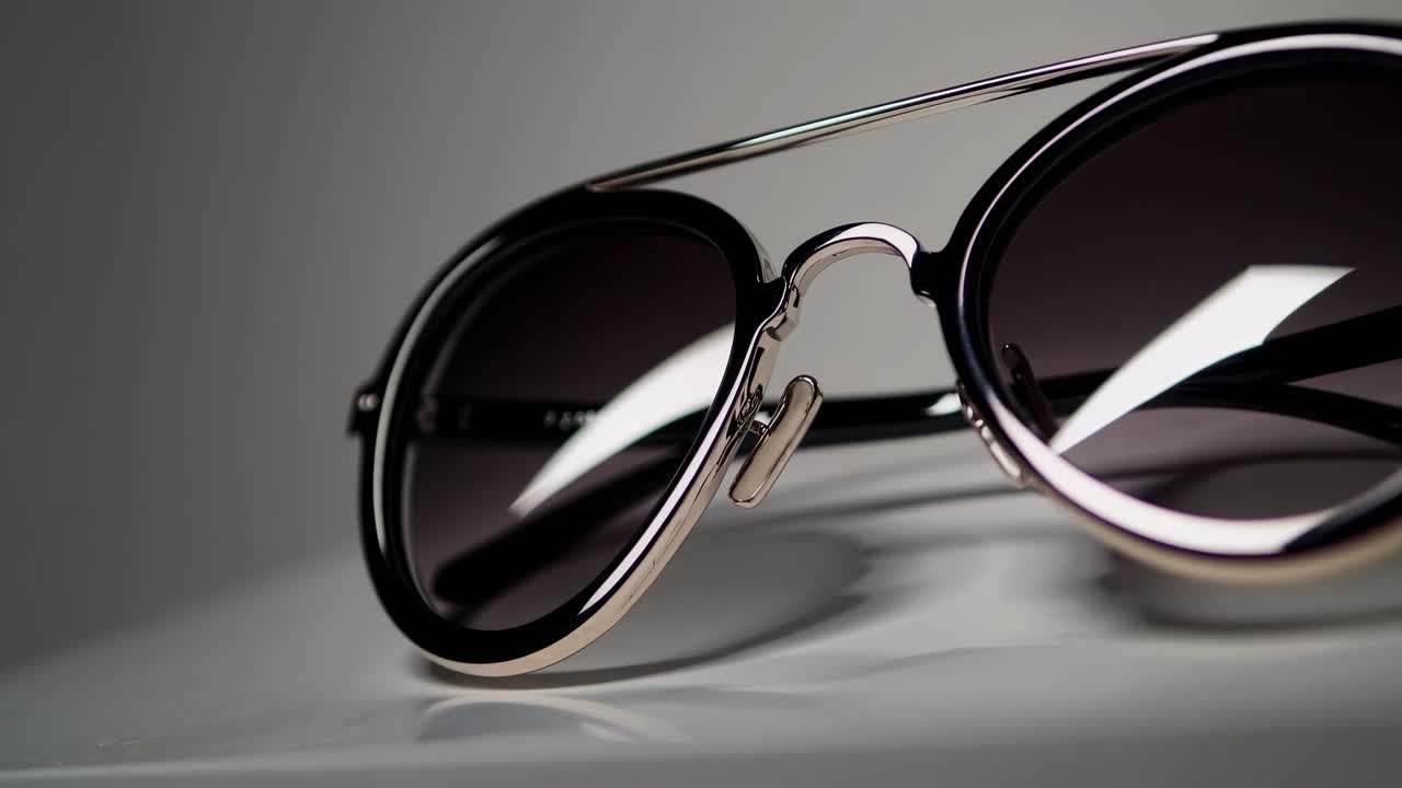 Video ravvicinato di occhiali da sole alla moda su una superficie bianca, che ne mette in mostra il design elegante e lucido