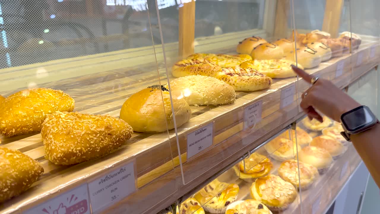 A customer selects bread from a well-lit bakery display in Bangkok, showcasing a variety of fresh baked goods