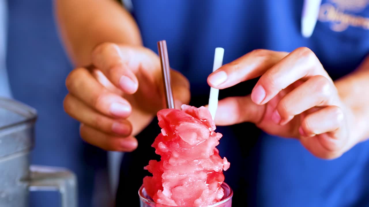 Hands skillfully prepare a watermelon ice drink with straws in a tall glass.