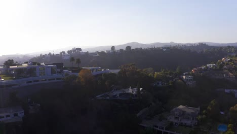 Toma-Aérea-Descendente-De-Mansiones-En-Una-Colina-En-Bel-Air-Con-Destello-De-Lente-Al-Atardecer