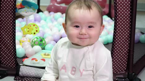 Infant-7-month-old-Happy-Baby-Girl-With-Chubby-Cheeks-Playing-next-to-Her-Playpen-smiling