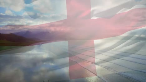Digital-composition-of-waving-england-flag-against-aerial-view-of-the-beach-and-sea-waves