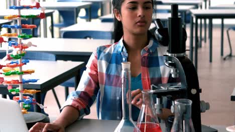Schoolgirl-experimenting-on-microscope-in-laboratory