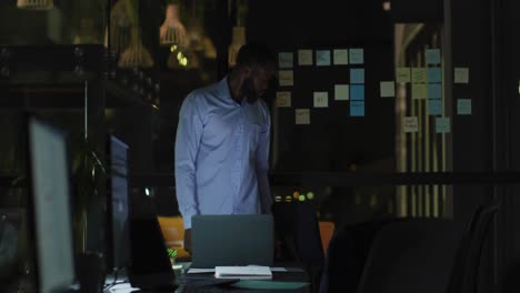 Video-of-tired-african-american-businessman-working-late,-leaving-laptop-and-office-desk-at-night