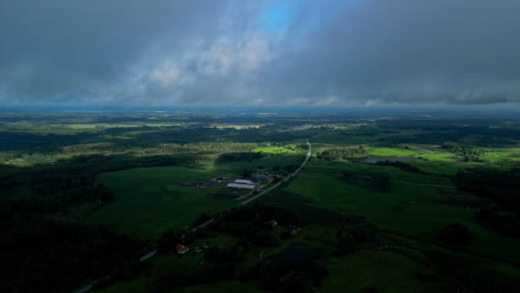 Beautiful-aerial-shot-of-lush-green-terrain-with-road-crossing-under-large-clouds