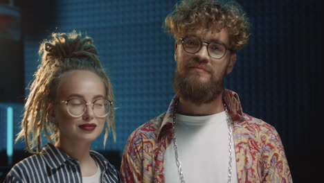 portrait shot of the stylish young man and woman in hipster style, singers of the duo looking at each other and then smiling to the camera in the sound studio