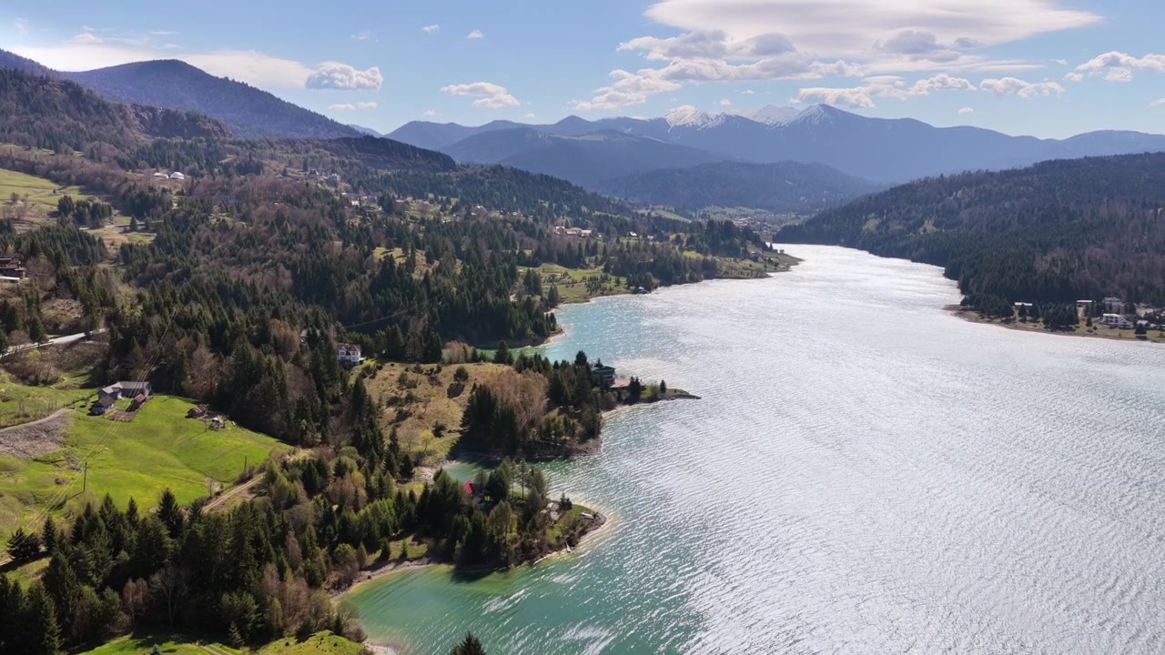 Veduta aerea con drone del lago Colibita con acque turchesi, circondato da colline boscose e case di montagna sparse