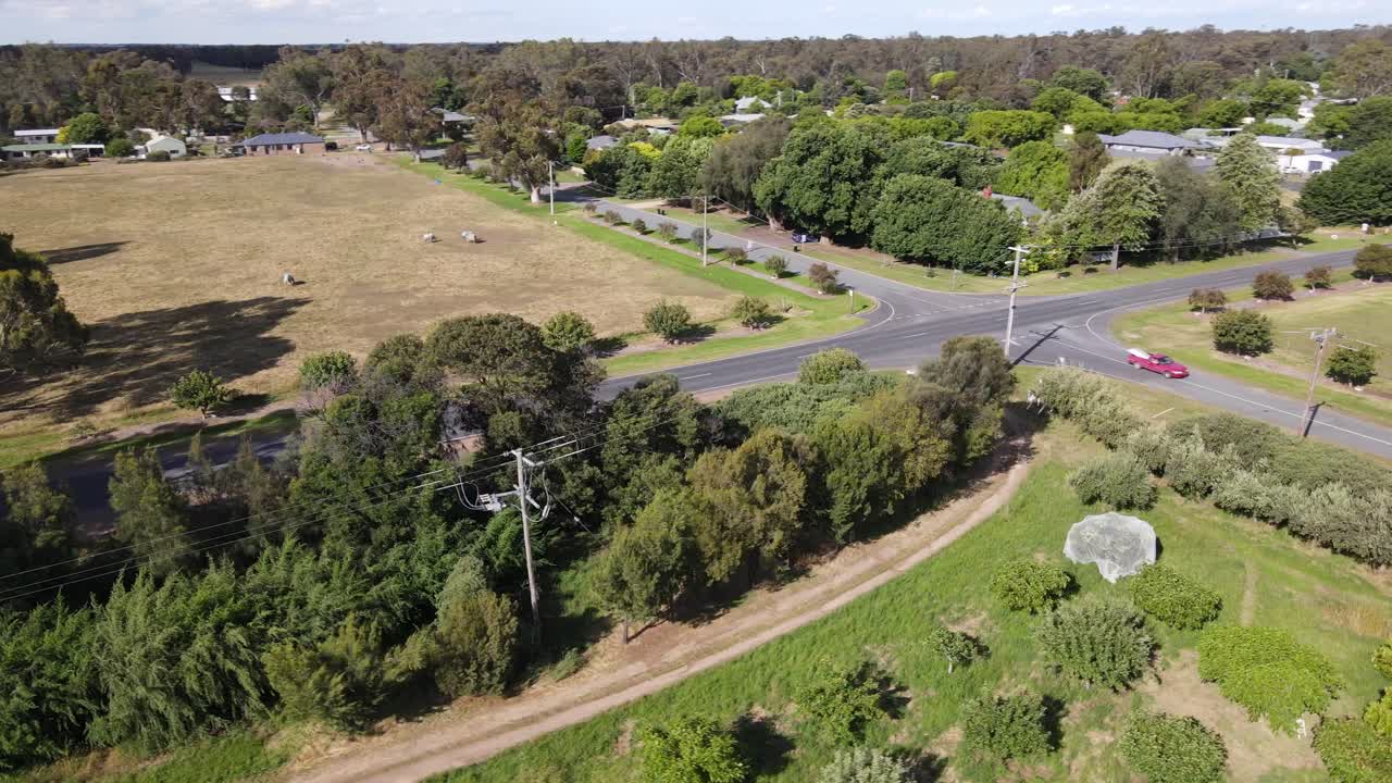 Vista aérea con dron sobre una granja de pueblo rural con carretera, líneas eléctricas y árboles verdes