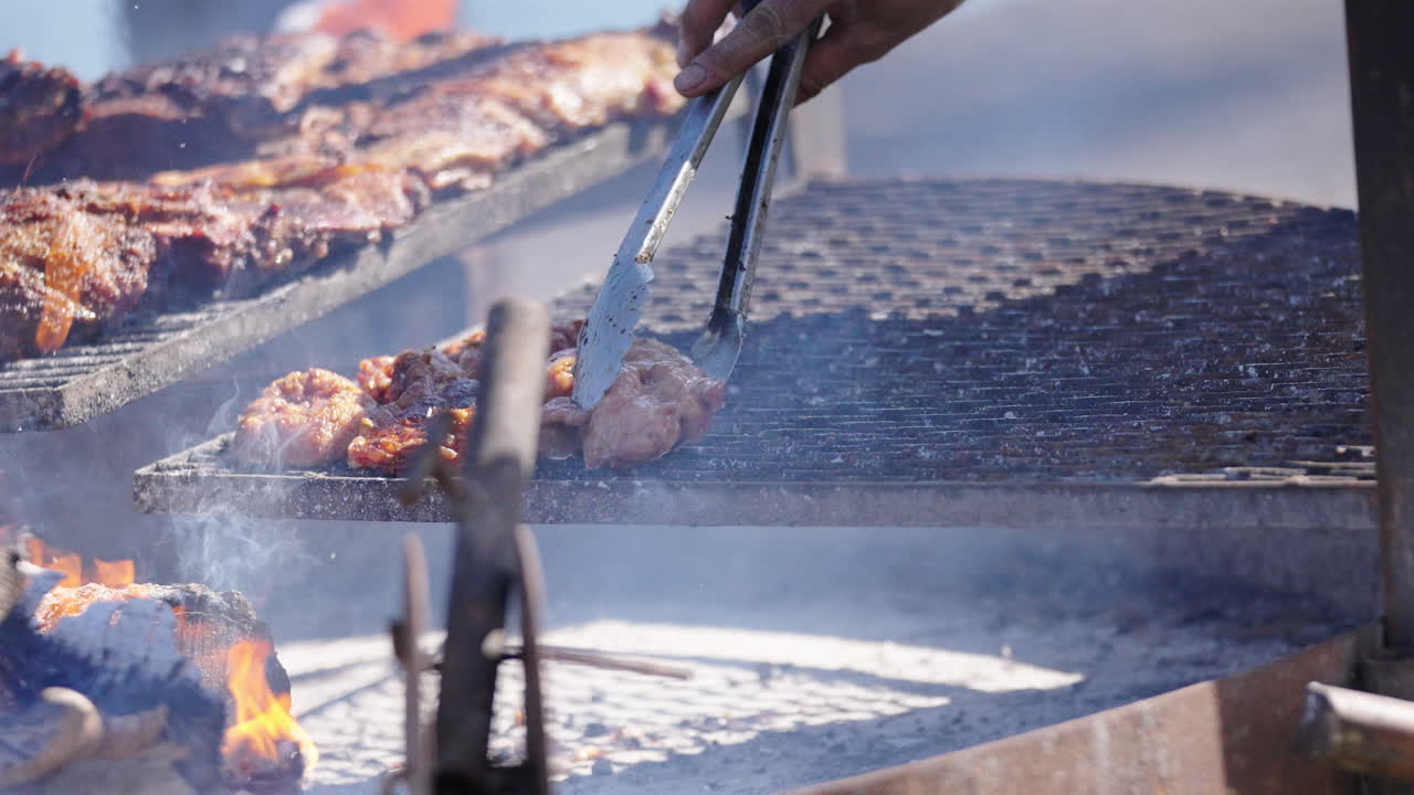 Juicy grilled meat being turned around for barbecue Asado Argentino with smoke rising.