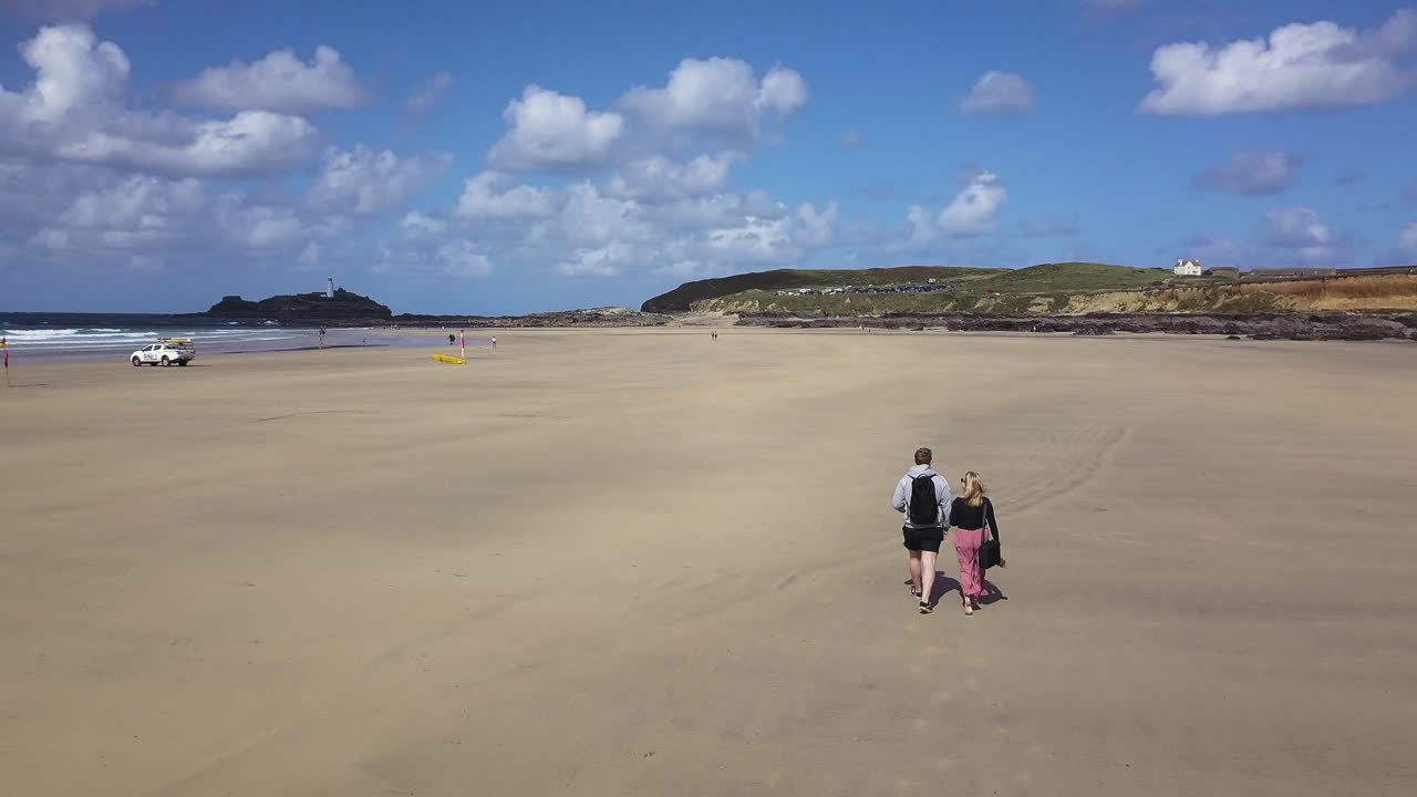 영국 콘월에 있는 고드레비 해변의 아름다운 해안을 따라 걷고 있는 관광 커플 - 드론 샷