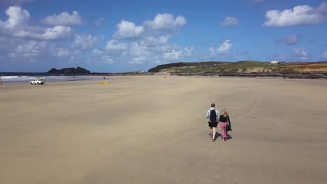pareja de turistas caminando por la hermosa costa de la playa de godrevy en cornualles, inglaterra - tiro con drones