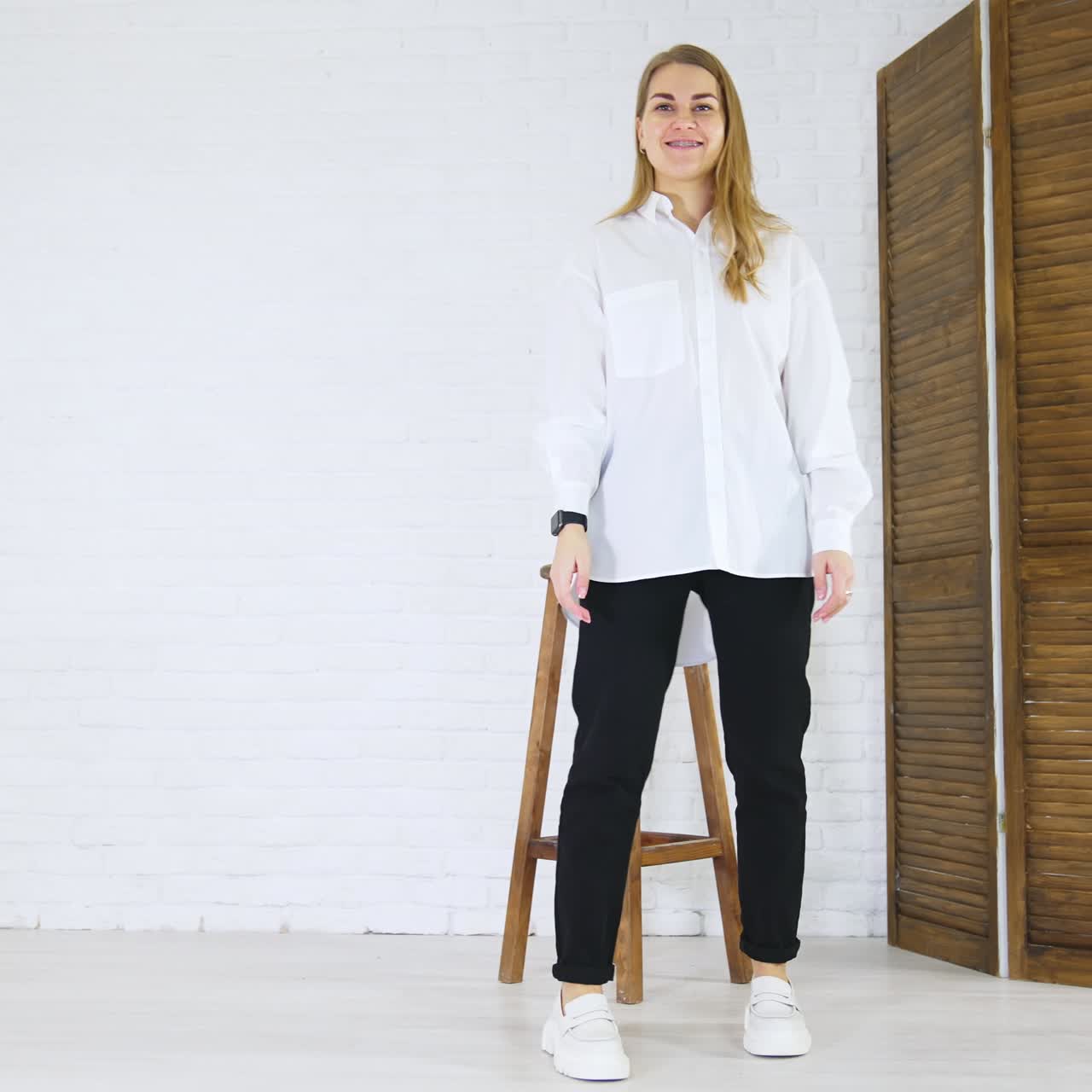 Blonde young woman demonstrates white shoes. Lady in white shirt and black pants walks back and forth showing footwear