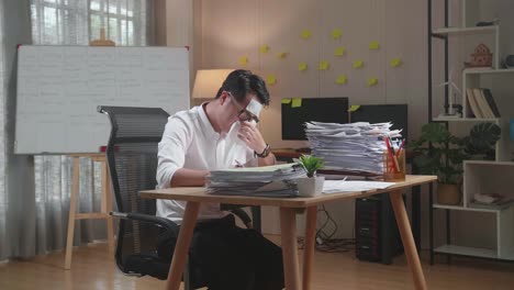 sick asian man having flu while working hard with documents at the office