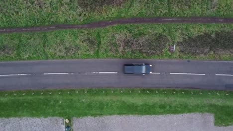 a slow descending top down shot of a road with a black car coming into frame on the left and exiting on the right