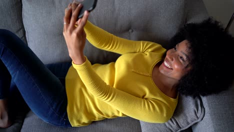 positive black woman taking selfie with smartphone on sofa